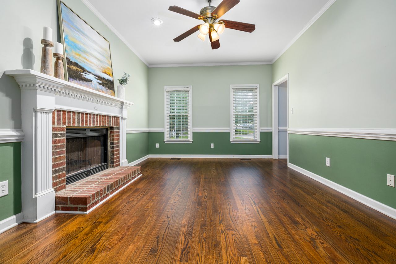 A cozy empty living room featuring a brick fireplace, wooden floors, and elegant decor.